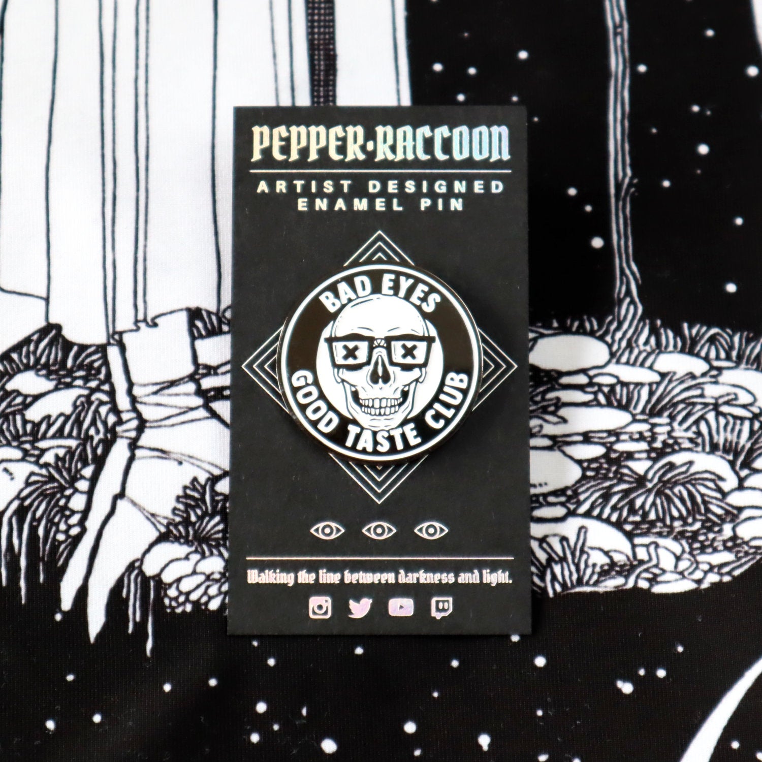 An enamel pin featuring a grinning skull wearing nerd glasses and the words Bad Eyes, Good Taste Club.