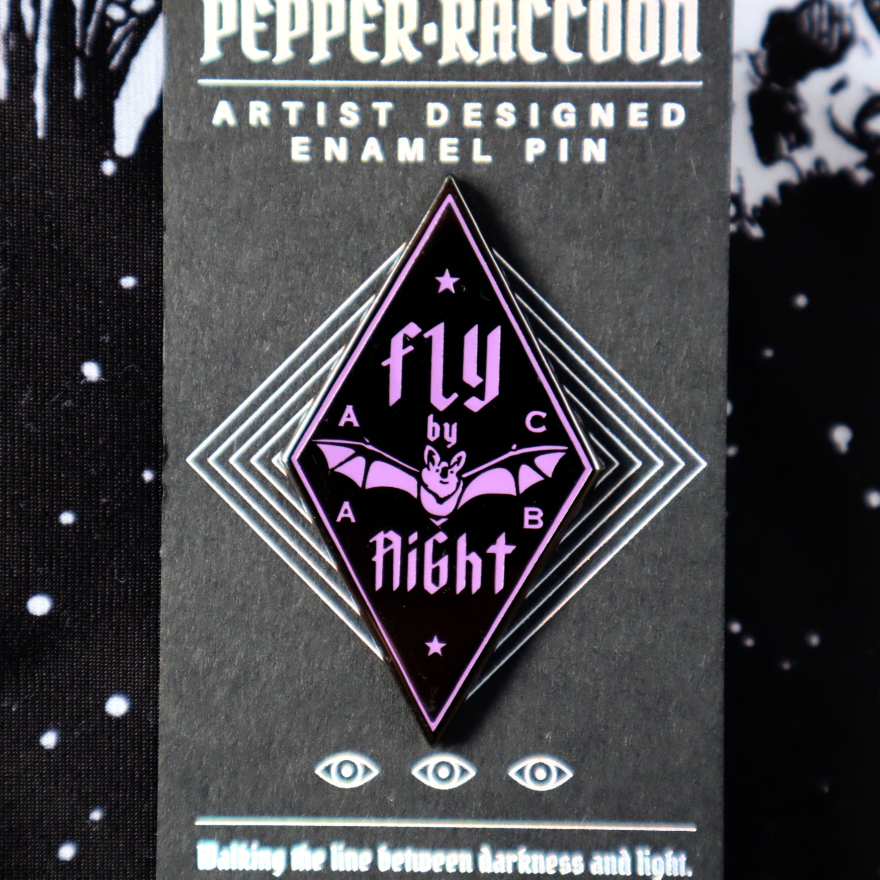 A diamond-shaped, black enamel pin with purple details, it says Fly By Night with a small NZ native bat or pekapeka emblazoned across the centre.