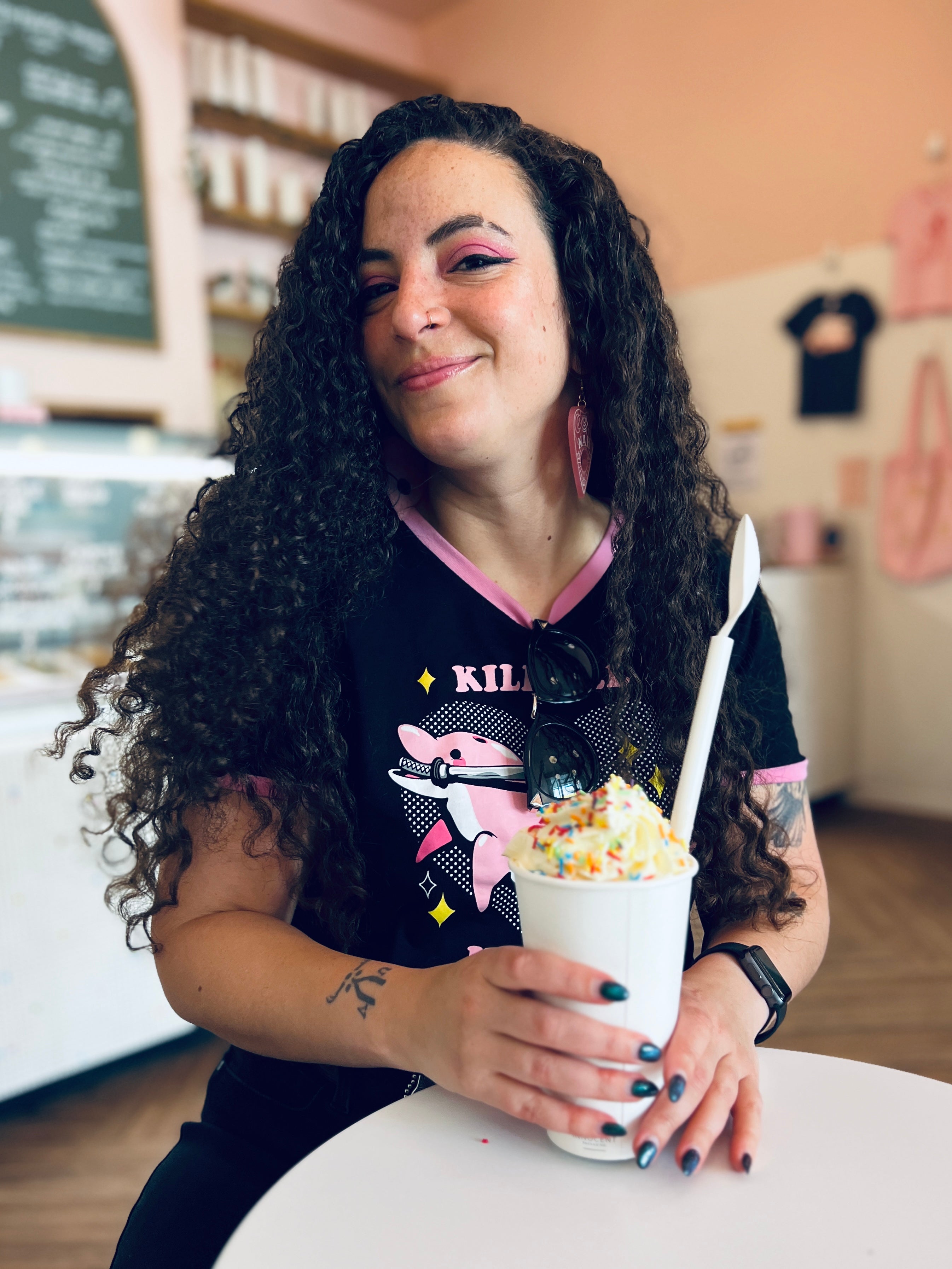 The artist Pepper Raccoon. She's holding a sprinkle covered milkshake and is smiling in an ice cream shop.