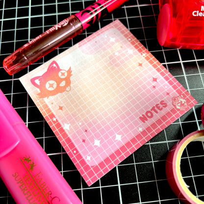 A flatlay of grid-layout sticky notes featuring a cute black cat sticking its tongue out and the word Notes. It is surrounded by similarly pink items.