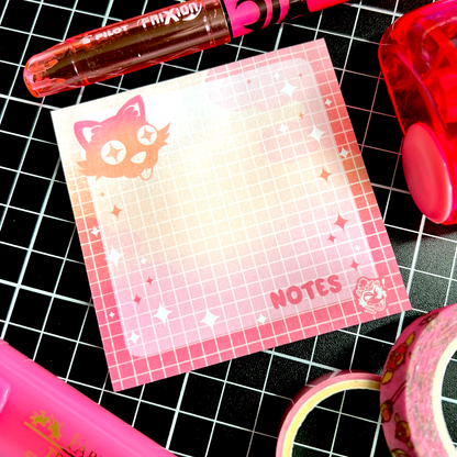 A flatlay of grid-layout sticky notes featuring a cute black cat sticking its tongue out and the word Notes. It is surrounded by similarly pink items.