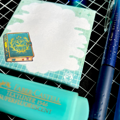 A blue-themed flatlay featuring a sticky note pad with a cloudy area for writing, background grids and fading colours, and an illustration of a spellbook.