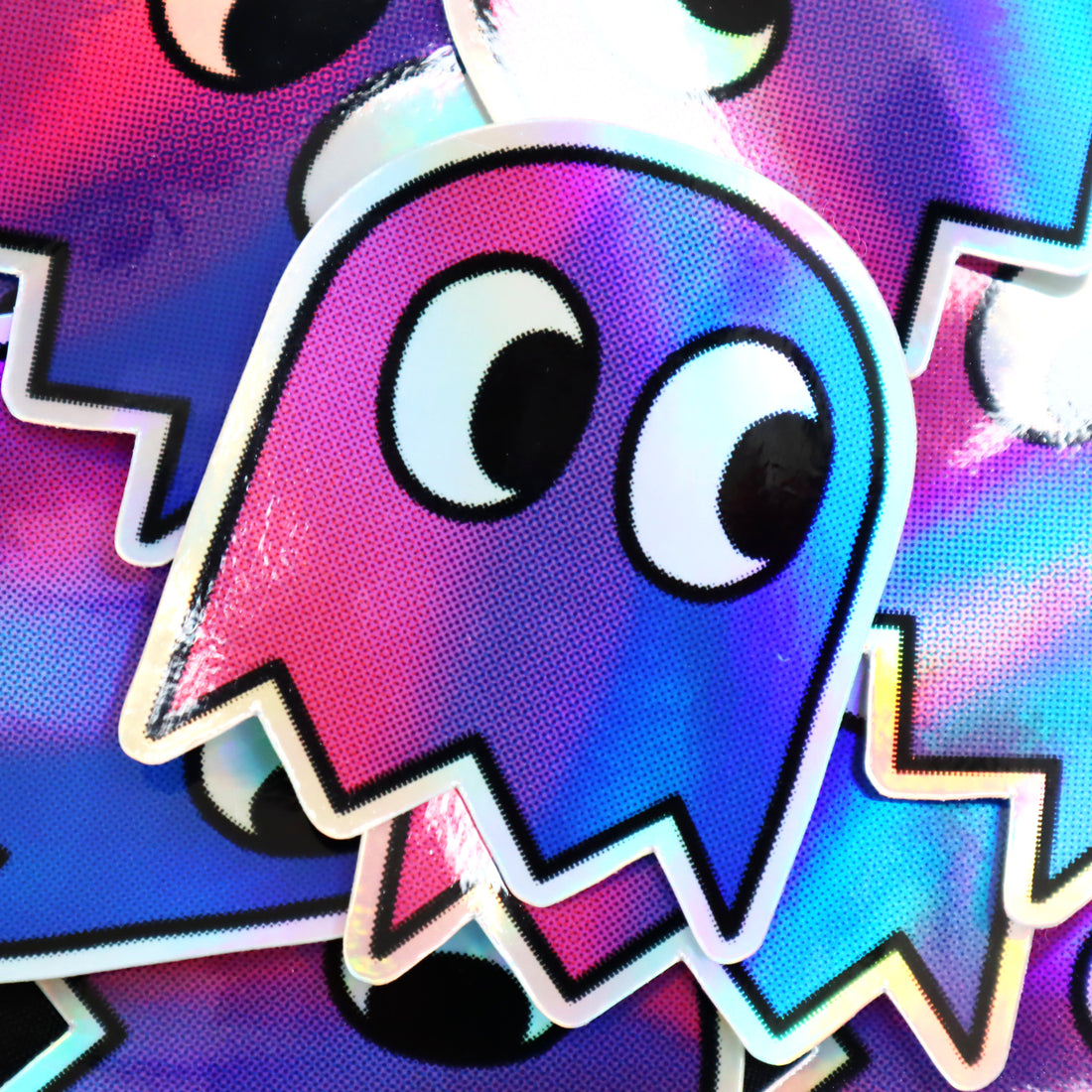 A bunch of holographic vinyl stickers, depicting a gamer-style pixel ghost in bisexual flag colours.